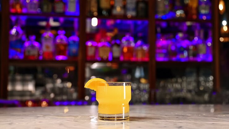 Cocktail all'arancia con fetta di agrumi sul bancone del bar. Cocktail all'arancia rinfrescante servito con fetta di agrumi su bancone da bar in marmo sotto luci al neon brillanti