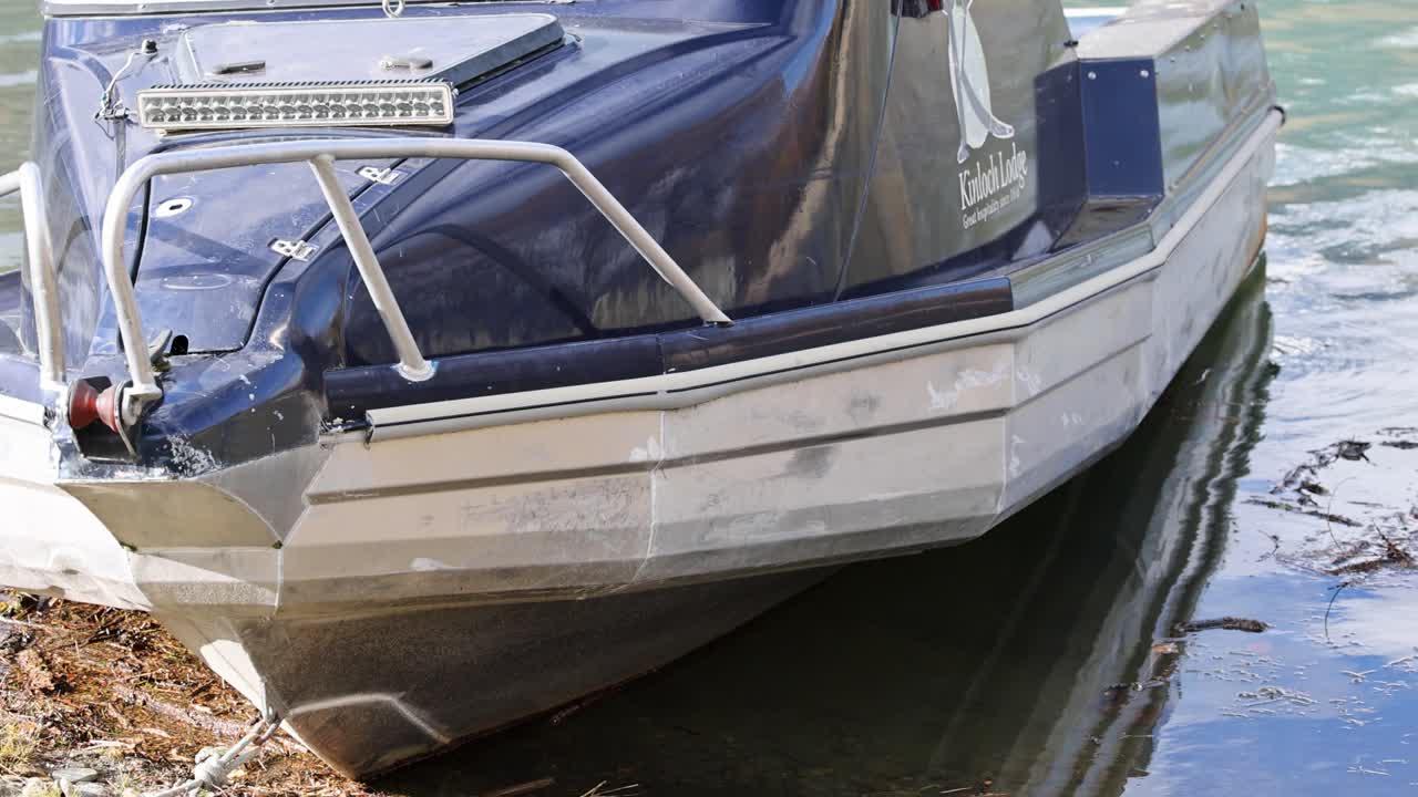 A stationary boat moored on a serene lake in Queenstown, captured in bright daylight with clear reflections