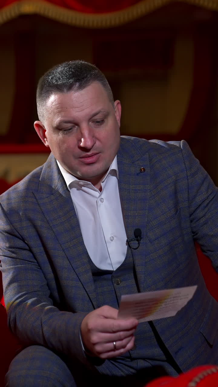 Man in costume reads a script. Medium shot of an actor rehearsing in empty theater among red chairs. Acting lifestyle. Vertical video