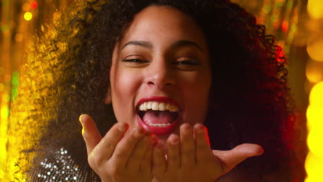 mujer joven celebrando en una fiesta o club soplando un puñado de brillo dorado hacia la cámara