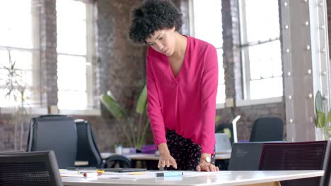 focused biracial casual businesswoman checking documents on table in office in slow motion