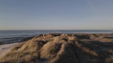 majestic sandy dunes with grass and horizon of ocean, aerial fly forward shot