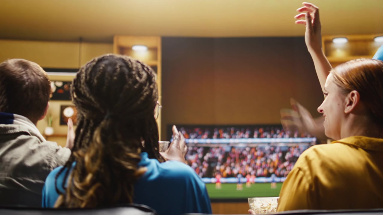 Close up of soccer fans holding popcorn bowl, ball and team scarves at home