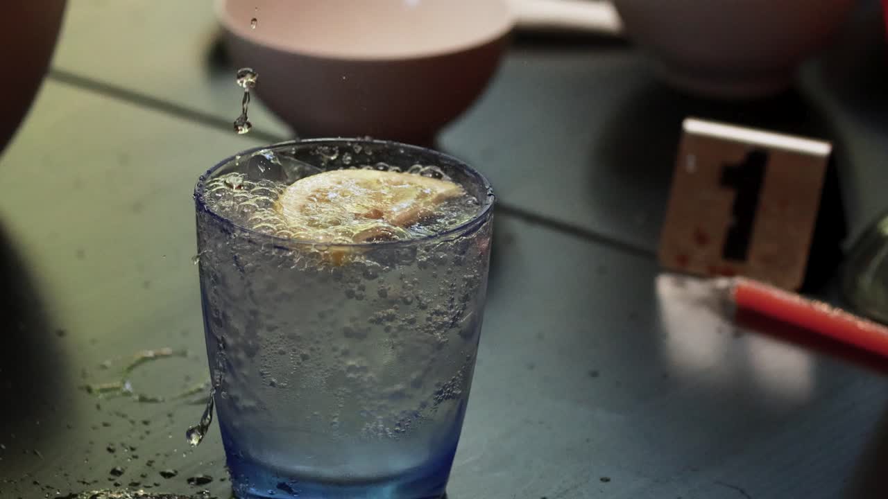A glass of soda with lemon slice and ice cubes, captured mid-pour, in a relaxed Phuket environment