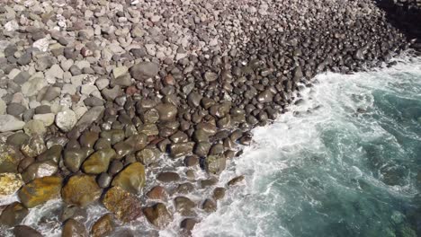 Langsame-Luftaufnahme-Der-Blauen-Wellen,-Die-In-Den-Strand-Aus-Kleinen-Steinen-Krachen