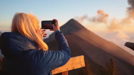 rubia, mujer filmando volcán activo con teléfono en guatemala