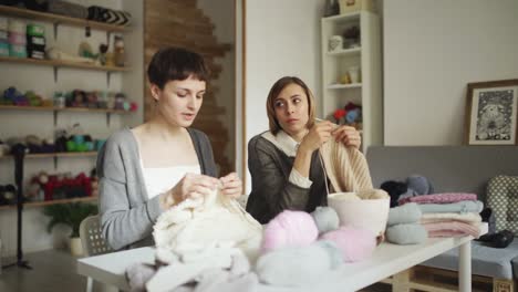 Two-woman-knitter-making-wool-fabric-sitting-at-table-in-textile-workshop