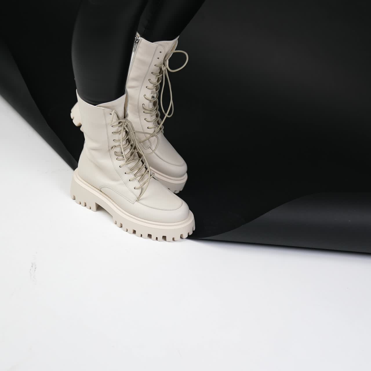 Milk-white tractor boots with laces demonstration. Female model in studio showing fashionable footwear