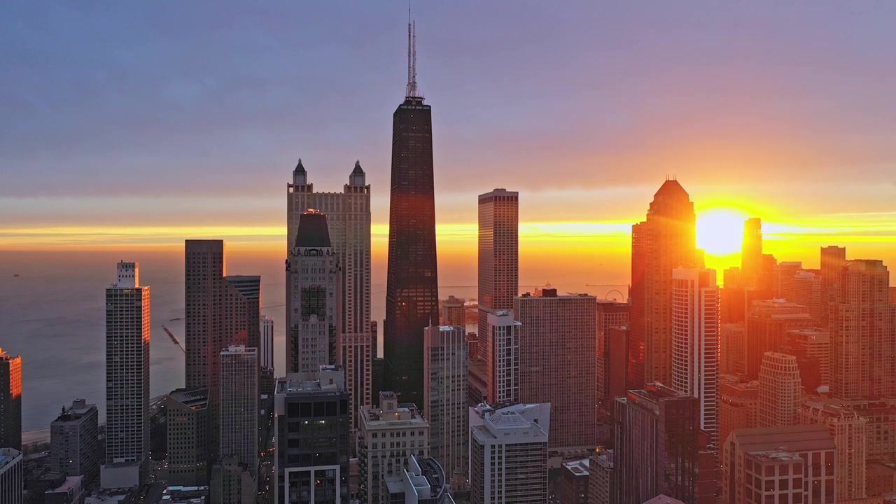 Movimento aéreo suave para cima revela o horizonte de Chicago brilhando sob um intenso nascer do sol dourado, com arquitetura densa do centro da cidade e o Lago Michigan ao fundo