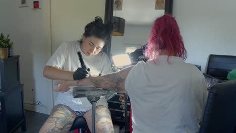 straight on view of female tattoo artist inking with precision a customer's forearm in a clean tattoo studio