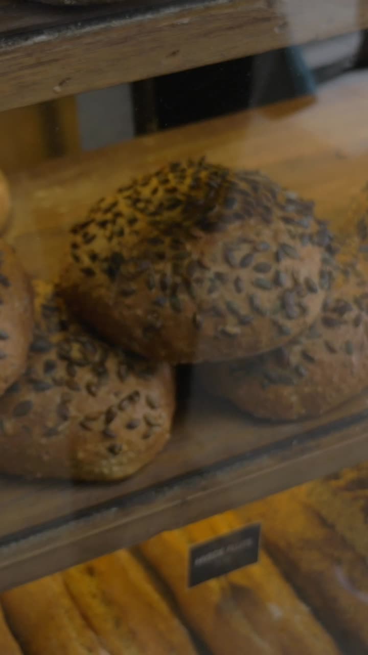 Customer Photographing Seeded Bread Rolls in a Bakery Display