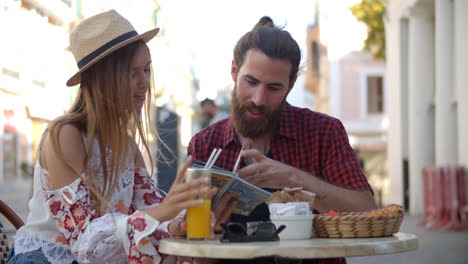 happy couple on vacation reading a guidebook outside a cafe