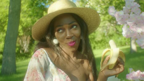 mujer negra comiendo tranquilamente disfrutando del plátano sonriendo en el parque dolly en primer plano