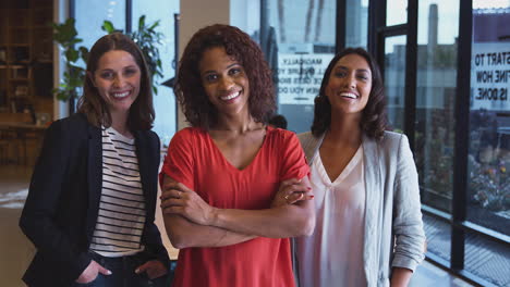 portrait of three businesswomen standing in modern open plan office together