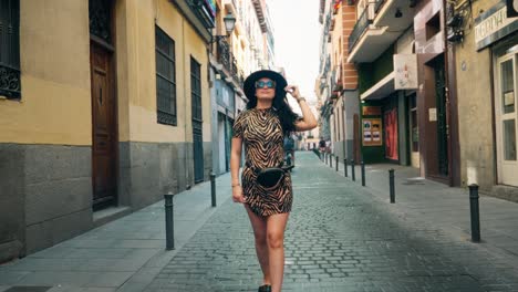 Chica-Caminando-Por-Las-Calles-De-España,-Edificios-De-Estilo-Antiguo,-Vestido-De-Chetah,-Con-Sombrero-Negro.