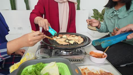 happy asian muslim family grilling beef slice on stove in korean bbq style and smelling the delicious aroma