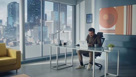 portrait of middle eastern businessman sitting at his desk working on laptop computer in big city office. successful digital entrepreneur plan investment strategy for e-commerce startup. full shot