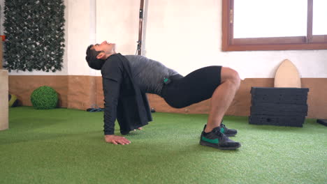 muscular man in jacket performing bridge exercise on artificial grass