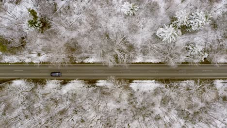 Volando-Sobre-Un-Automóvil-Que-Conduce-Un-Dron,-Siguiéndolo-Cuando-Conduce-A-Través-De-Un-Paisaje-Forestal-Invernal