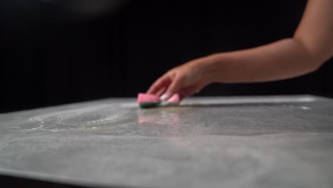 la mujer usa una esponja rosa y agua con jabón para limpiar y limpiar la mesa gris.