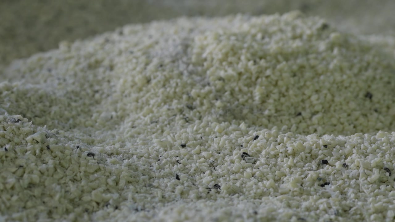 Primo piano estremo a livello del suolo di un mucchio di granuli di plastica riciclata con texture fine e macchie scure sparse.