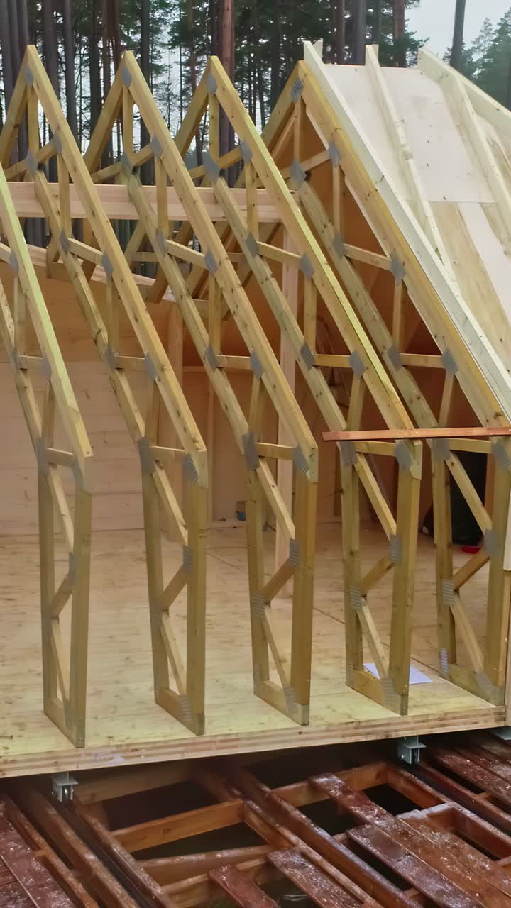 Drone pulls back to show framed house under construction in forest clearing at sunset