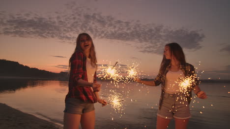 a group of friends girls and men dance on the beach with sparklers in slow motion at sunset. celebrate new year on the beach