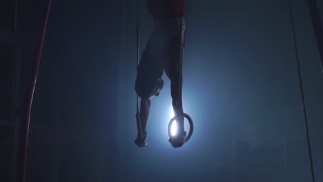 gymnast on a dark background stands on his hands using rings in the air. performs rotation in the olympic program in slow motion 120 fps. gymnastic rings, professional gymnast