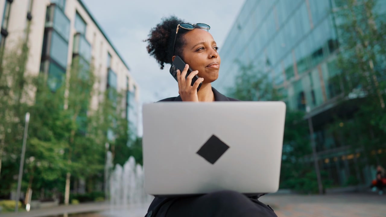 Professional Woman Working on Laptop and Talking on Phone Outdoors