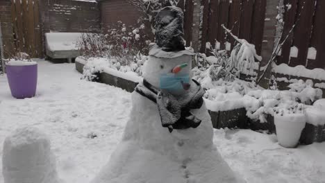 funny snowman wearing face mask on winter backyard during snowy day