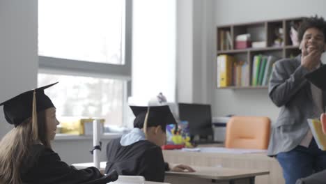 kid high-fiving one of his classmates. they are wearing gowns and mortarboards.