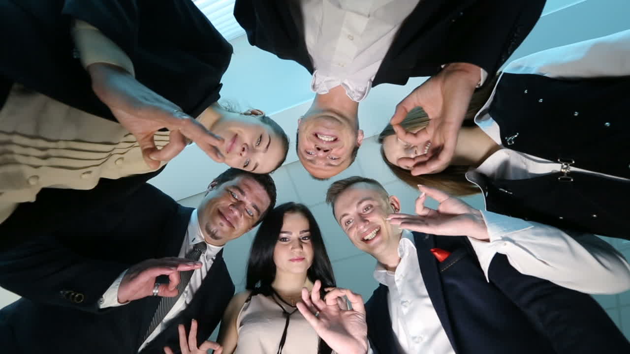 Business Team Is Showing Ok Sign. Beautiful business team is showing Ok sign, looking at camera and smiling while standing in office