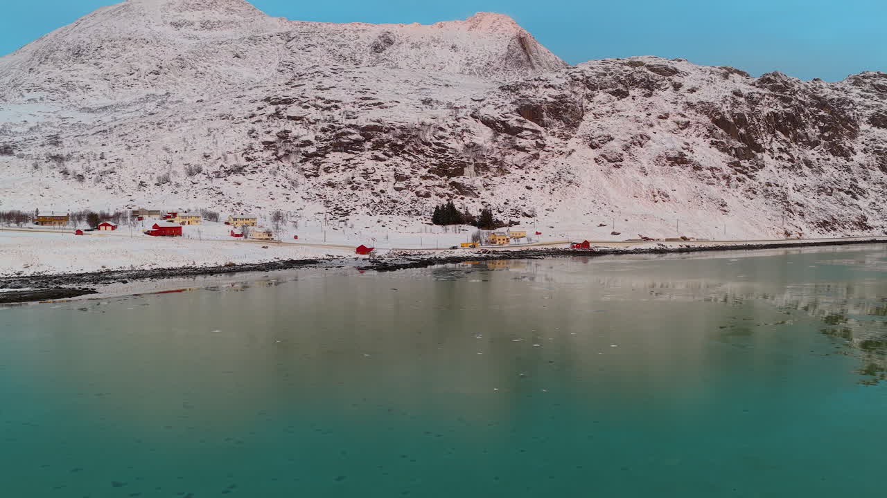 Una splendida ripresa cinematografica di montagne innevate nelle Lofoten, Norvegia, che si riflettono nelle calme acque turchesi di un fiordo durante l'inverno