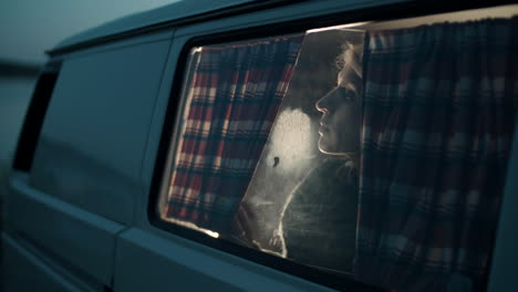 Woman-Looking-through-Window-of-Camper-Van-in-Evening