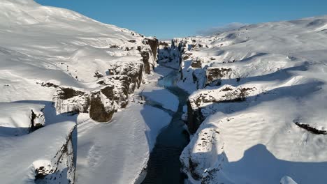 aerial view of a glacier river flowing through a canyon covered in snow, on a sunny day