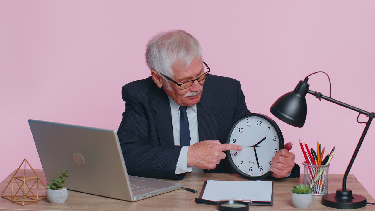 Senior smiling businessman showing time on wall office clock, ok, thumb up, good approve success
