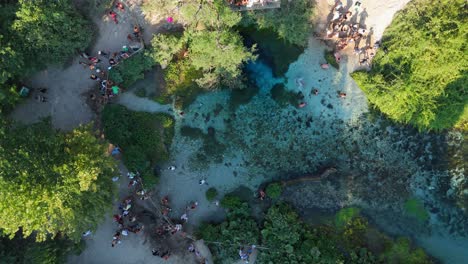 tourists swimming and exploring the vibrant blue eye water spring in albania, aerial view