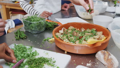 primer plano de una mujer cortando y agregando hierbas frescas al plato en la clase de cocina de la cocina