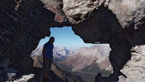 hiker touching rock admiring view trough hole arch on mountain walking away kananaskis alberta canada