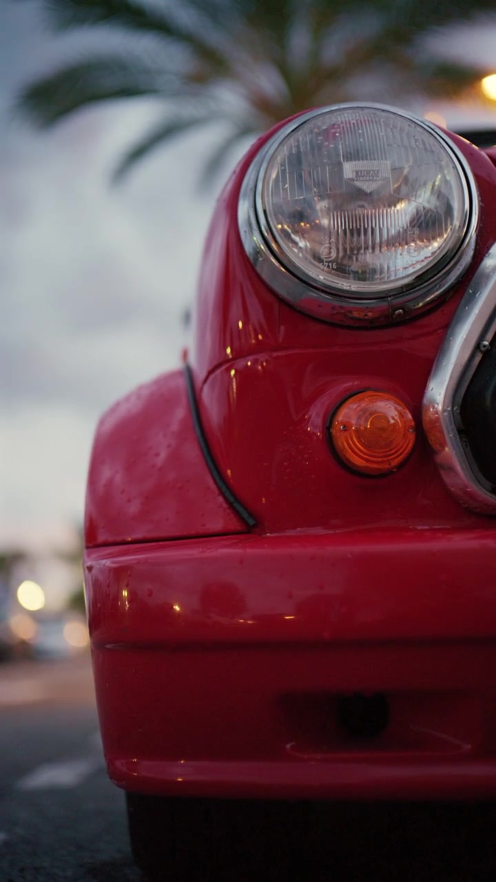 Kino-Nahaufnahme eines roten Oldtimer-Scheinwerfers und einer geschwungenen Motorhaube mit verschwommenem Straßenhintergrund, der den Retro-Automobilstil an der französischen Riviera einfängt