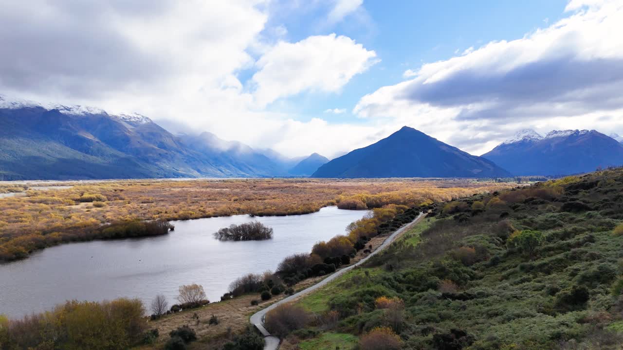 Aerial view of Glenorchy's serene landscape featuring a lake, mountains, and lush greenery under a partly cloudy sky