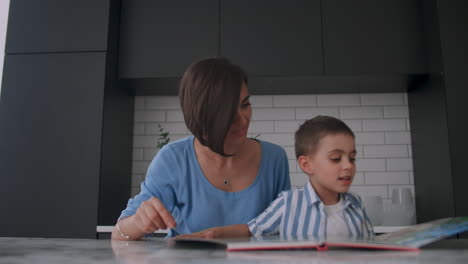 una joven madre española con su hijo sentado a la mesa enseña a leer al niño ayudando y incitando a su hijo