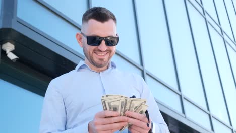a man in sunglasses is smiling while holding a wad of money in his hand near a glass building a rich