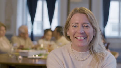 portrait of a blonde middle aged woman looking at camera and smiling while spending time with her family during a party at home