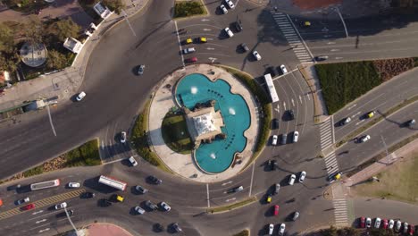 Aerial-top-down-showing-spraying-fountain-of-La-Carta-Manga-Monument-with-driving-cars-at-roundabout-during-sunset---Buenos-Aires-City,Argentina