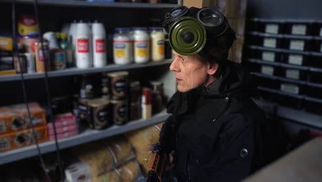 pensive doomsday prepper sitting alone in a nuclear fallout bunker wearing a gas mask and holding a submachine gun