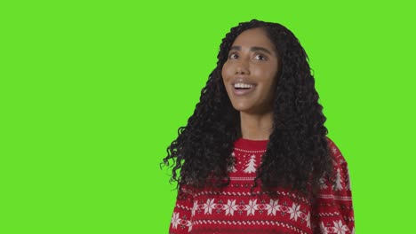 studio portrait of woman wearing christmas jumper against green screen with hands out to catch falling snow