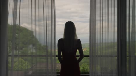 silueta de mujer despertando y saliendo del balcón de la cabaña, cortinas balanceándose lentamente en el viento