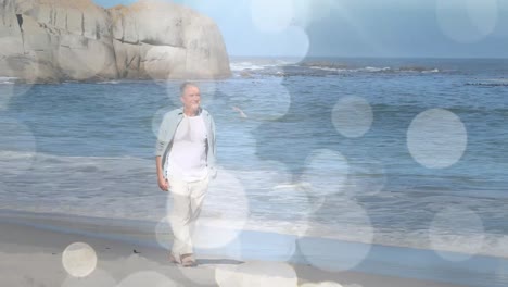 animation of glowing lights over a sad senior caucasian man walking on the beach