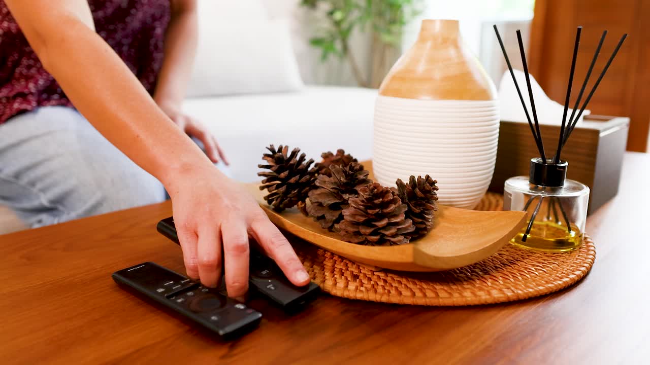Una mano posa delicatamente due telecomandi neri su un tavolo di legno con oggetti decorativi.
